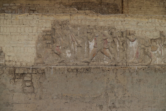 Fragment of an ancient Moche adobe wall featuring a faded relief frieze with stylized figures from the procession of captives at Huaca Cao Viejo in Peru