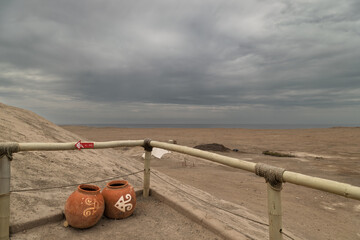 Decorated terracotta clay pots on a sandy path with the Pacific Ocean and desert landscape in the background at El Brujo, Peru © simonmayer