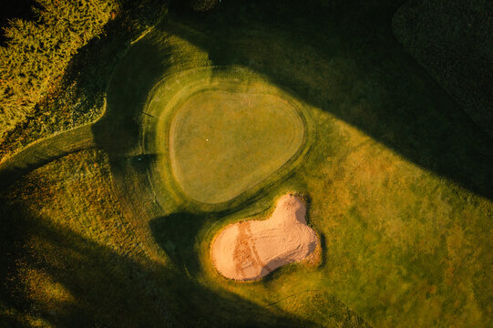 Aerial view of a golf course green and sand bunker illuminated by golden hour light with long shadows in Valmiera, Valmiera, Latvija.