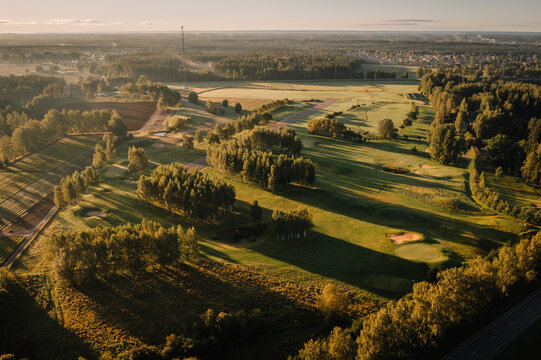 Aerial view of a golf course featuring green fairways, sand bunkers, and long tree shadows during golden hour in Valmiera, Valmiera, Latvija.