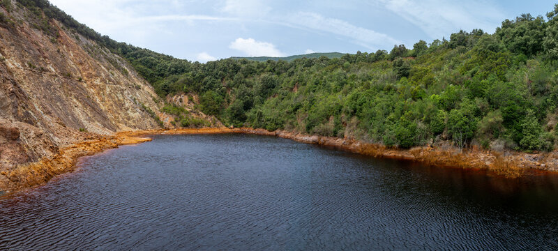 Aerial view of the Laghetto delle conche, a striking lake with dark mineral-rich water surrounded by steep cliffs and lush vegetation in Rio Marina, Toscana, Italy.