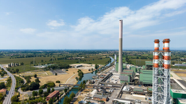 Aerial view of the Tavazzano con Villavesco power station with tall chimneys and industrial infrastructure near a canal in rural Tavazzano con Villavesco, Lombardy, Italy.