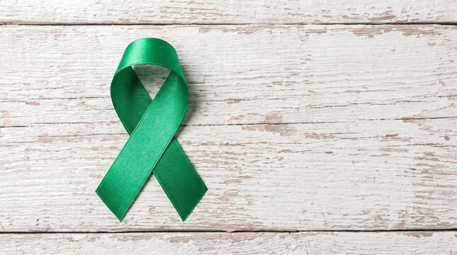 Green awareness ribbon on white wood background for mental health, organ donation, and environmental causes. Rustic top view symbol for healthcare campaigns and medical advocacy.