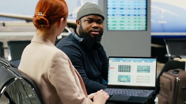 A business CEO and assistant evaluate company data and KPIs in an airport lounge, comparing the financial situation while traveling together for a global business trip before departure.