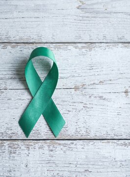 Green awareness ribbon on white wooden background for mental health, liver cancer, and organ donation. Rustic style with copy space for healthcare campaigns.