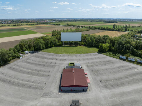Aerial view of a drive-in cinema with a large white screen and empty parking spaces surrounded by green fields and trees in Aschheim, Bavaria, Germany.