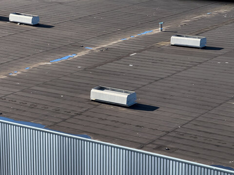Aerial view of a flat industrial building roof featuring several white ventilation units and small puddles of water in Leeuwarden, Friesland, Netherlands.