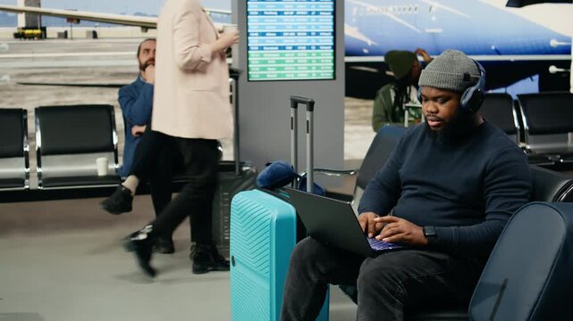 African American digital nomad works on a laptop near an airport gate with a suitcase while waiting for international departure on a business trip.