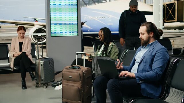 Entrepreneur types on a laptop and checks a mobile phone screen impatiently in an airport lounge, waiting for important notifications during a delegated business trip before departure.