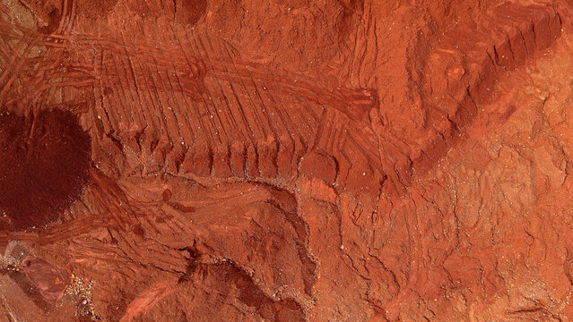 Aerial view of red laterite soil with excavation patterns, heavy equipment tracks, layered earth textures, and rugged industrial terrain. Abstract landscape with copy space.