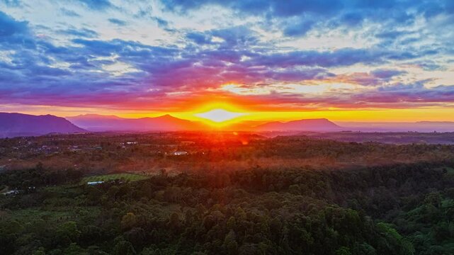 A breathtaking sunrise illuminates a small village nestled among lush green fields and karst mountains, with vibrant clouds filling the sky. The harmony of rural life set dramatic natural formations