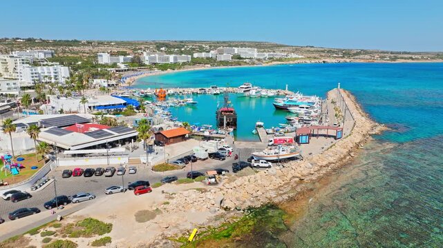 Drone view of Ayia Napa Harbour and coastline in Cyprus. The harbour entrance, clear blue water and rocky shore shape a scenic seaside panorama.