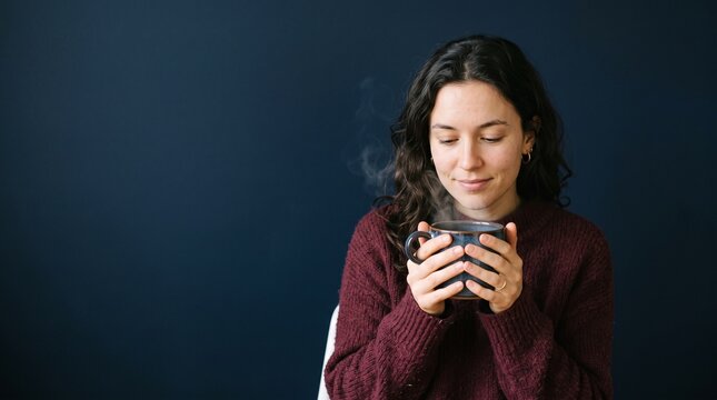 Woman enjoying a warm cup of coffee or tea with steam rising on a dark blue background
