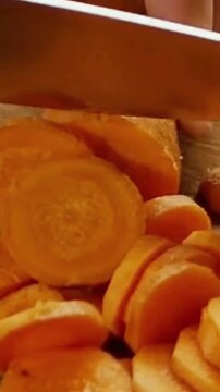 Close-up of a chef slicing fresh raw carrots on a wooden board