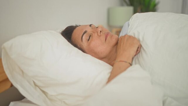 Woman smiling and hugging pillow in bedroom, lying on white duvet with hand showing ring and bracelet; serenity morning comfort.