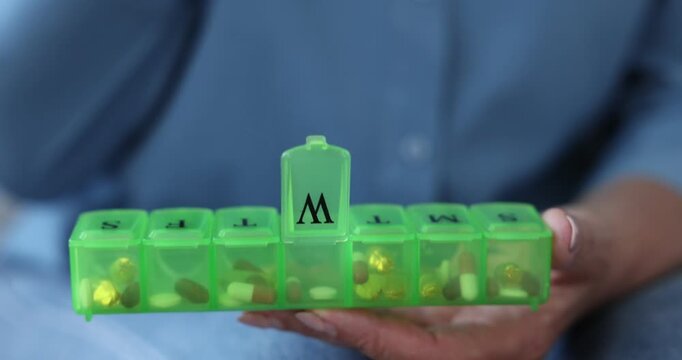Senior woman taking pill out of organizer at home, closeup. Camera moving in