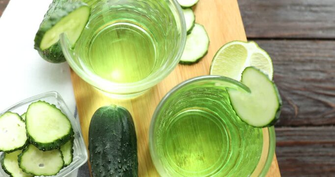 Cucumber juice in glasses, fresh vegetables and lime pieces on table, rotating
