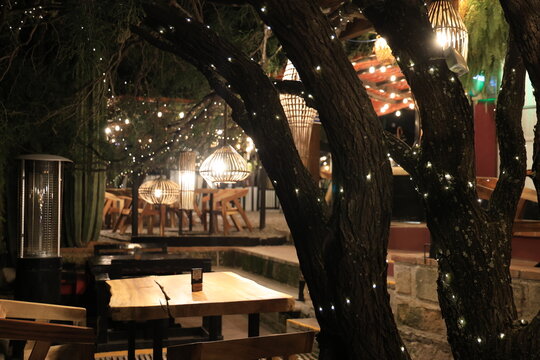 Terraza exterior de restaurante acogedor decorada con luces c&aacute;lidas y mesas de madera
