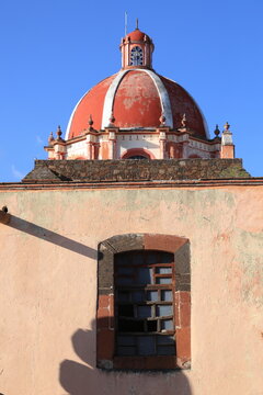 C&uacute;pula de iglesia colonial y fachada r&uacute;stica con ventana de madera en M&eacute;xico