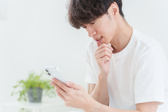 悩みながらスマートフォンを使う若い男性