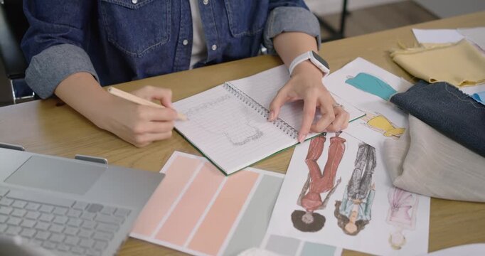 Female designer referencing color chips, sketching and comparing fabrics, finalizing design at desk