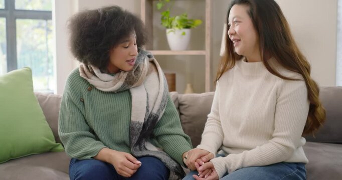 Two women sitting on couch, speaker opening up, adjusting scarf, listener holding hand, comforting