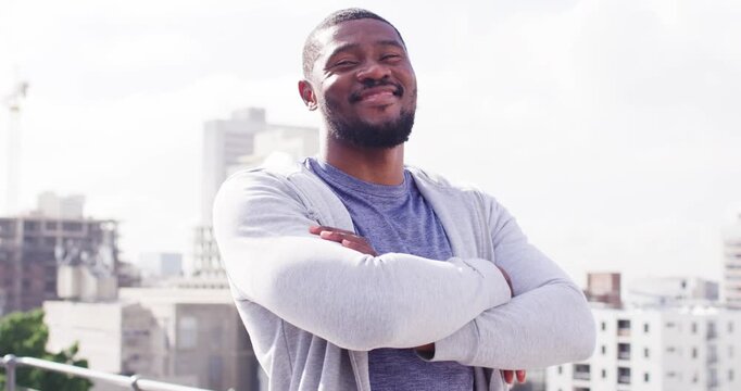 Mid-adult African man posing for camera adjusting hoodie crossing arms laughing by roof railing
