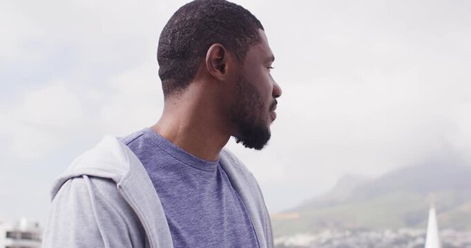 Man standing on rooftop viewing skyline and spire, turning head, squinting, reflecting gray hoodie