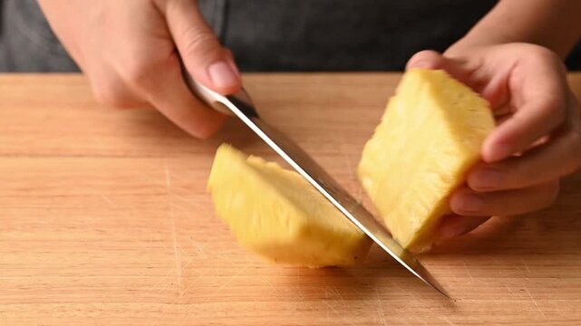 Close up of woman hands using knife to cut fresh pineapple on a wooden cutting board
