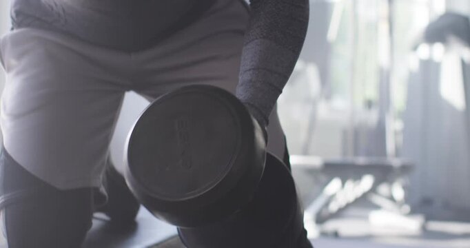 Fit male kneeling on bench, reaching for 25KG dumbbell, rowing and lowering for back strength