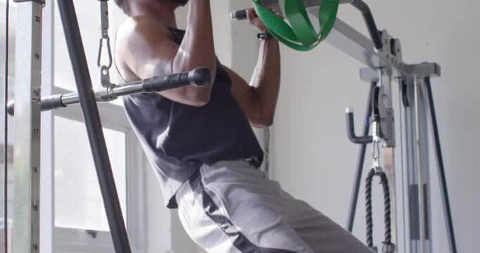 Man doing pull-ups with green band looped over bar at gym, wearing tank for strength