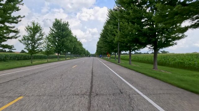 Vehicle point of view shot driving along a paved access road approaching a small university campus in the distance. Captured at University of Illinois Springfield.