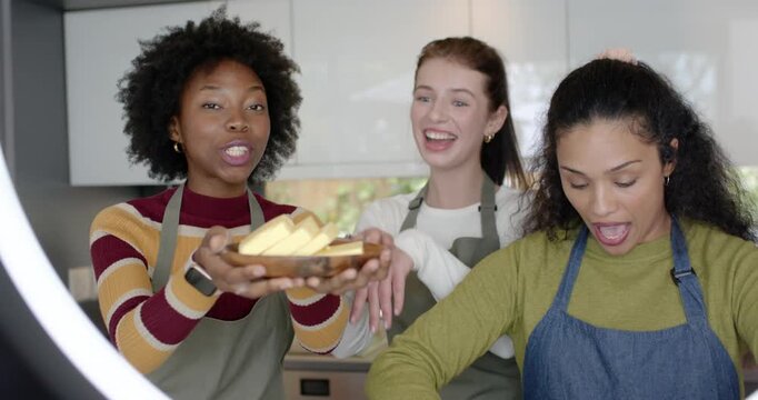 Diverse female friends left presenting butter, center clapping, right holding eggs, stirring batter