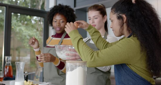 3 women in aprons ring light camera signaling cracking eggs and mixing batter at kitchen counter