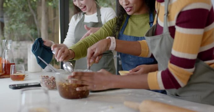 Three women friends leaning at counter scooping pecan filling onto tray for baking after left cue
