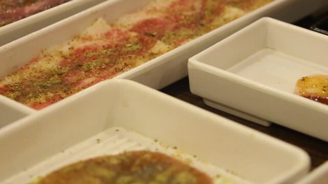 A close-up video shot of thin slices of raw, spice-marinated beef on a serving tray, ready to be grilled at an atmospheric Asian-style restaurant.