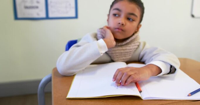 African American child writing notebook in classroom with two pencils pausing thinking leaning head