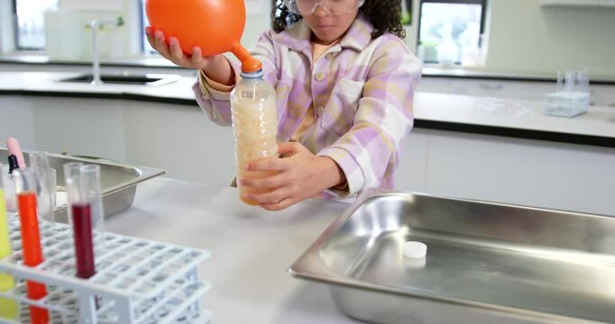 African American child performing reaction creating gas, inflating balloon on bottle in school lab