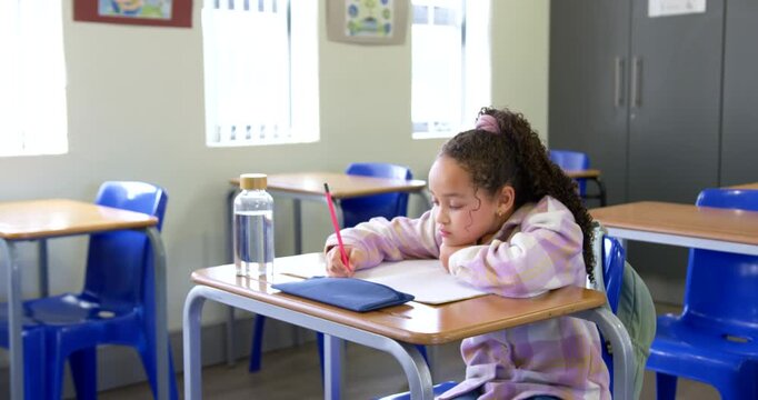 African American child with red pencil, writing in open notebook at front desk to finish work