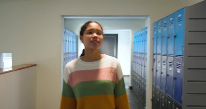 Asian girl child walking through school hallway after class, opening locker and retrieving backpack