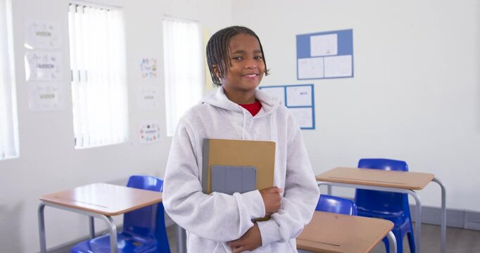 Youth student shifting gaze as camera moves, smiling holding brown folder, gray tablet in classroom