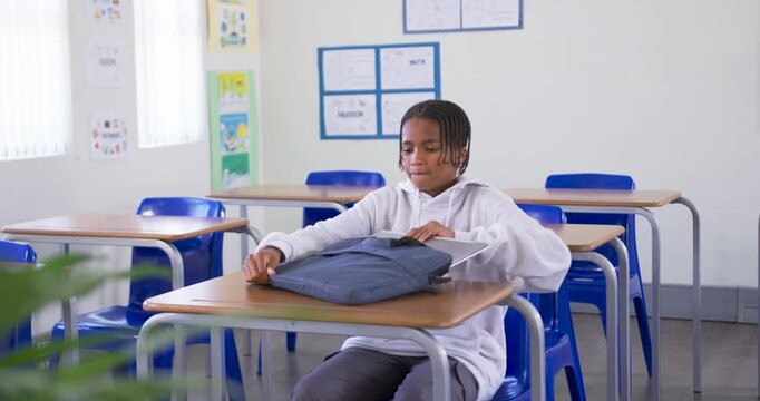 Teen African American in hoodie preparing for class pulling laptop from sleeve typing at desk