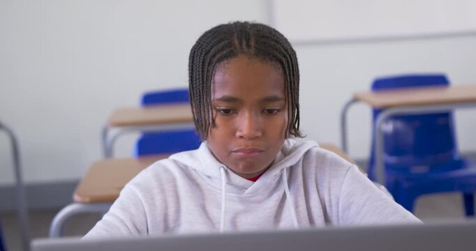 African American male youth touching laptop, scanning screen, relaxing and smiling at school desk