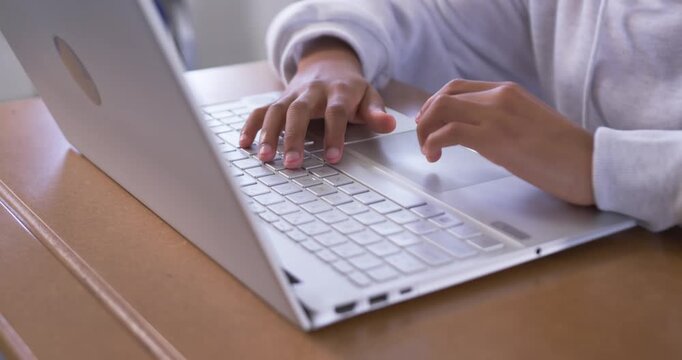 African American youth male typing silver laptop in classroom, camera pulling back, studying