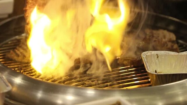 Juicy beef steaks sizzling on a Korean BBQ grill with dramatic smoke and flames, creating an authentic gourmet dining experience in a premium restaurant setting.
