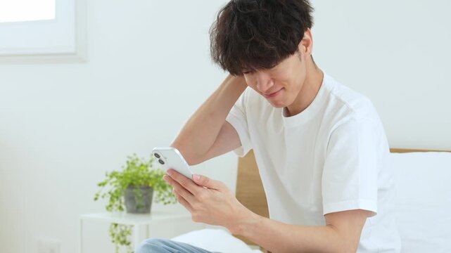 悩みながらスマートフォンを使う若い男性
