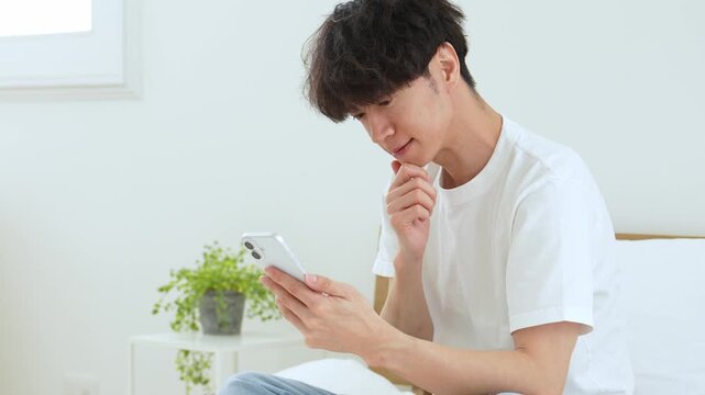 悩みながらスマートフォンを使う若い男性
