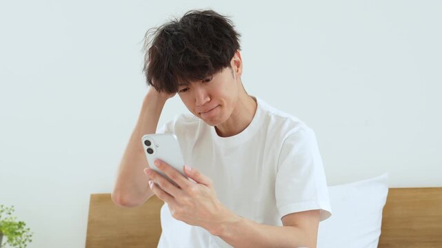 悩みながらスマートフォンを使う若い男性
