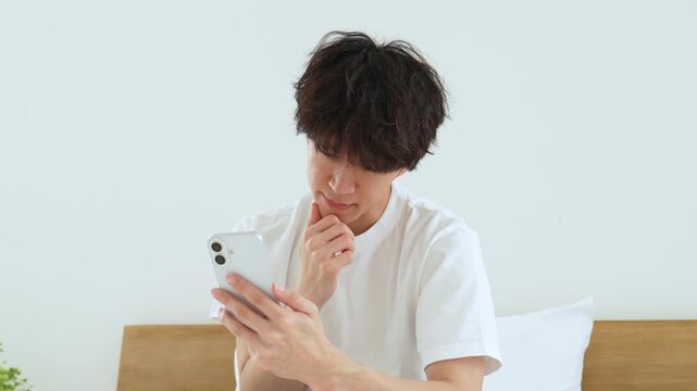 悩みながらスマートフォンを使う若い男性
