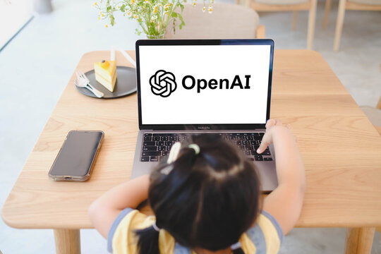 Bangkok, Thailand. July 19, 2026; An overhead view of a young child touching a MacBook Pro laptop displaying the OpenAI logo on a white screen at a wooden table.